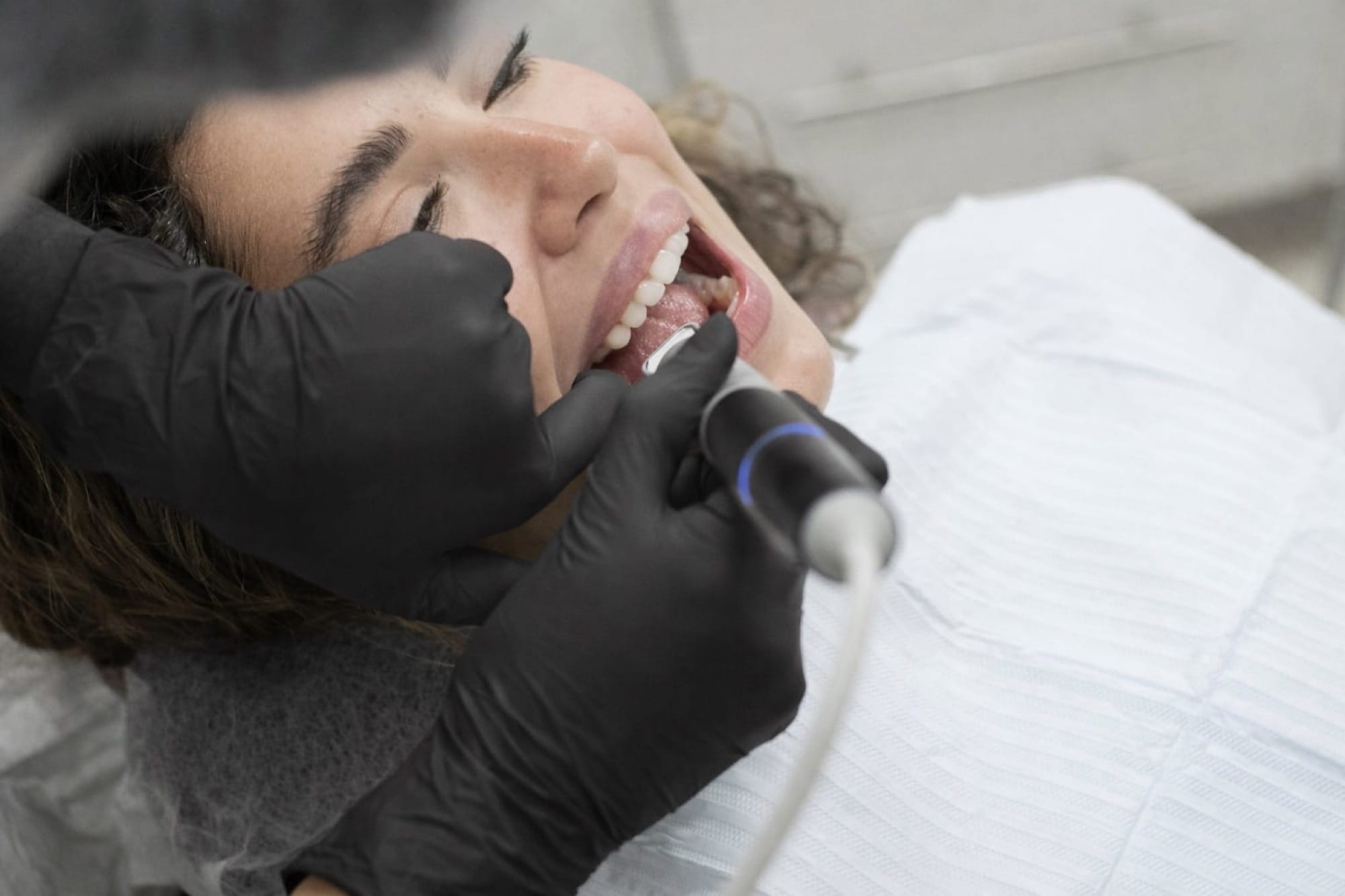 Patientin bei Zahnbehandlung: Eine Frau liegt im Behandlungsstuhl, während ein Zahnarzt mit rotierendem Instrument die Zähne behandelt.