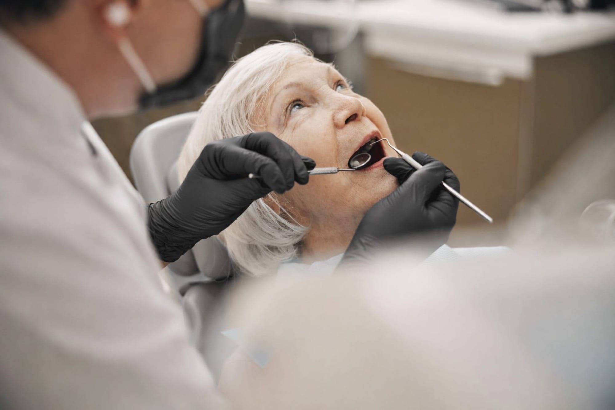 Zahnärztliche Behandlung bei älterer Patientin: Eine Seniorin wird im Behandlungsstuhl mit Instrumenten untersucht.