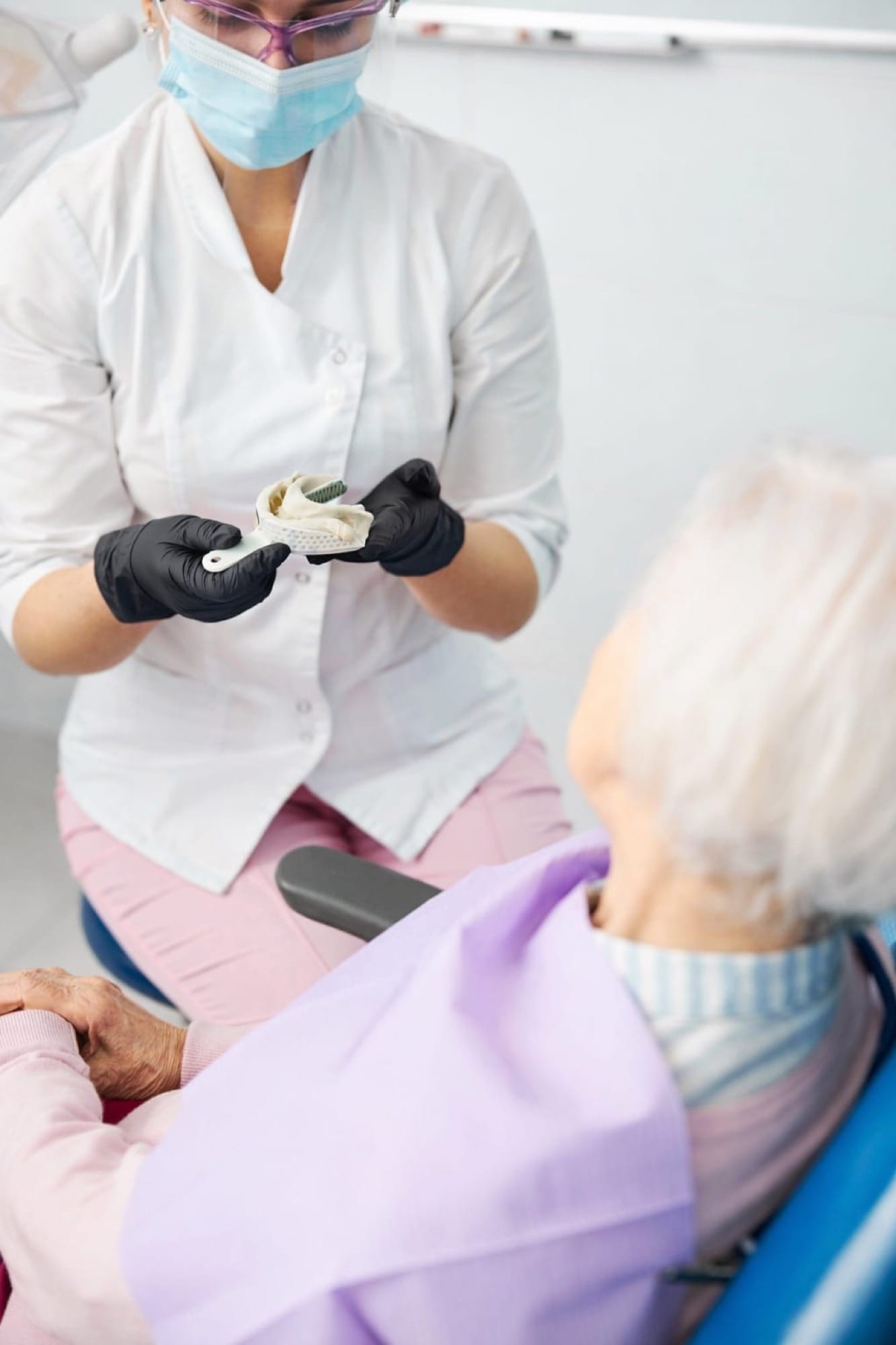 Zahnarztbehandlung aus Perspektive: Ältere Patientin im Stuhl, während medizinisches Personal eine Abdrucknahme der Zähne vorbereitet.