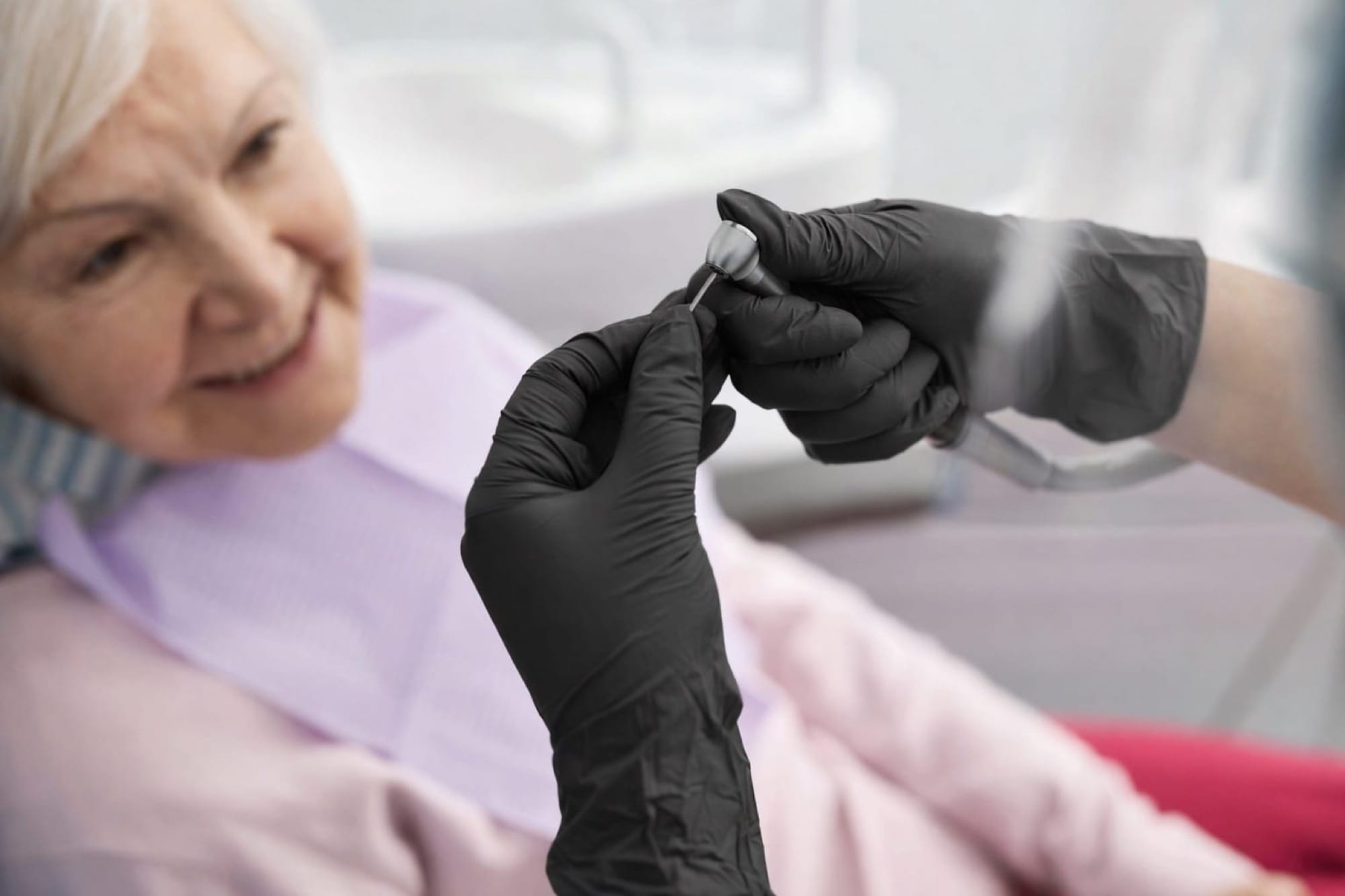 Seniorin bei Zahnbehandlung: Eine ältere Frau sitzt entspannt im Stuhl, während ein Instrument vorbereitet wird.