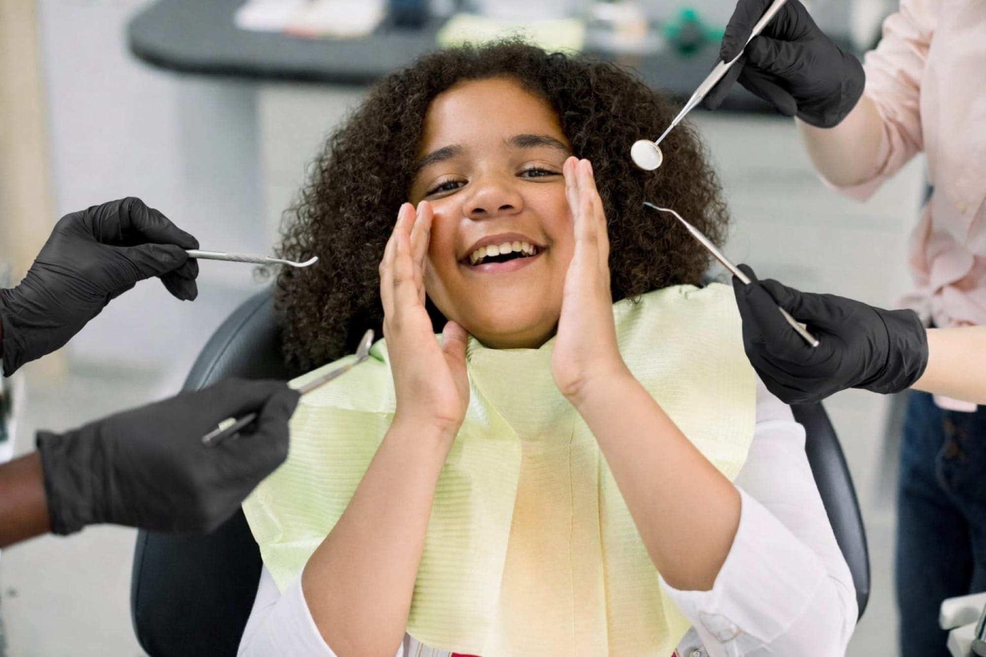 Kind beim Zahnarztbesuch: Ein fröhliches Mädchen sitzt im Behandlungsstuhl und reagiert spielerisch auf die Untersuchung.