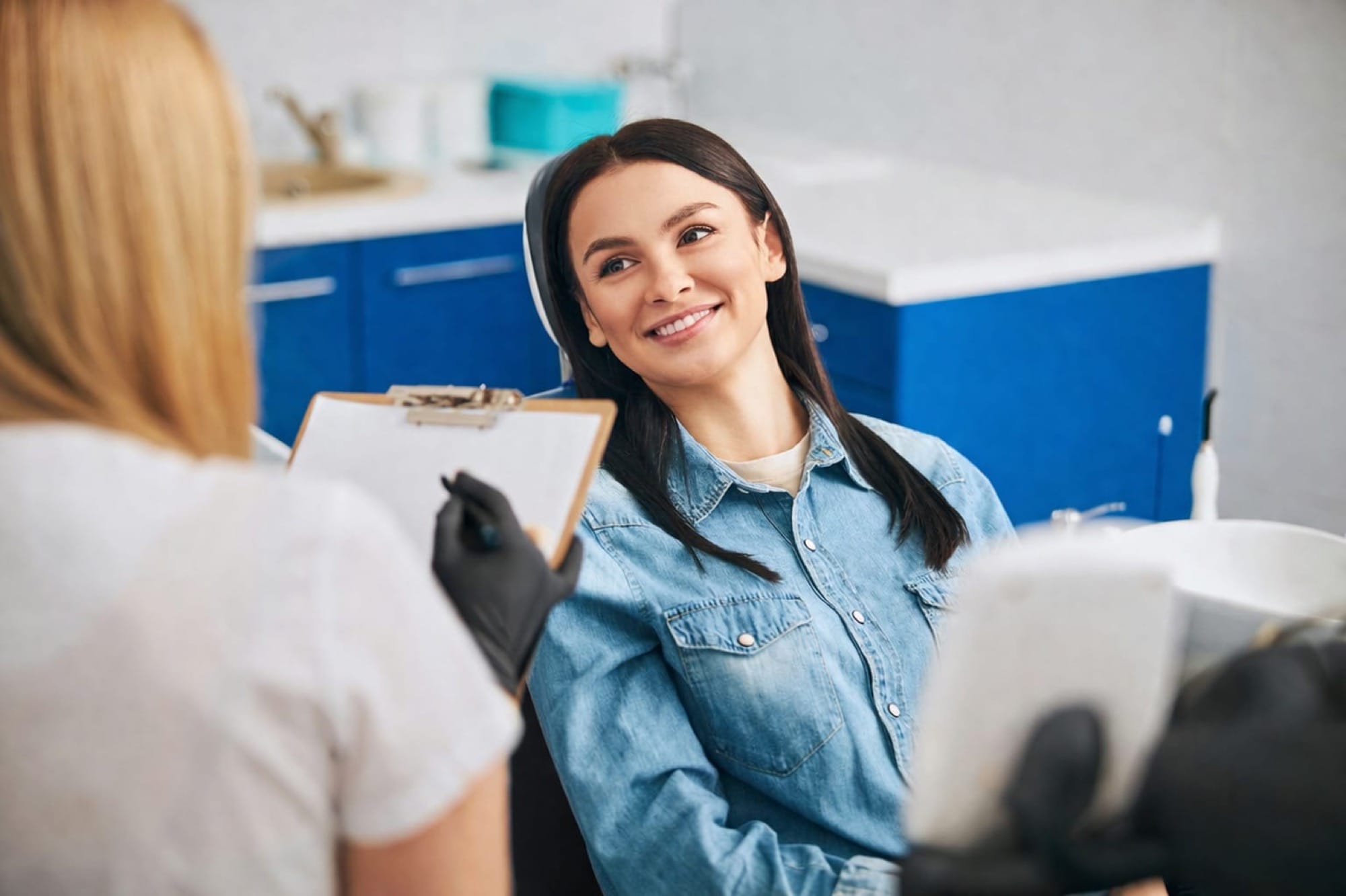 Zahnärztliche Beratung: Eine Frau sitzt entspannt und hört aufmerksam zu, während eine Fachkraft Behandlungsschritte erklärt.